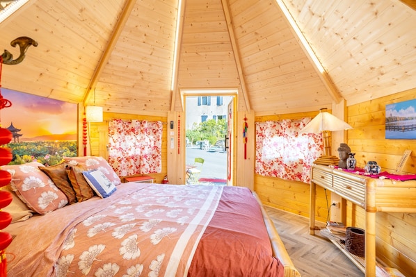 Une chambre avec un lit, des murs en bois, un bureau et une vue sur l’extérieur.