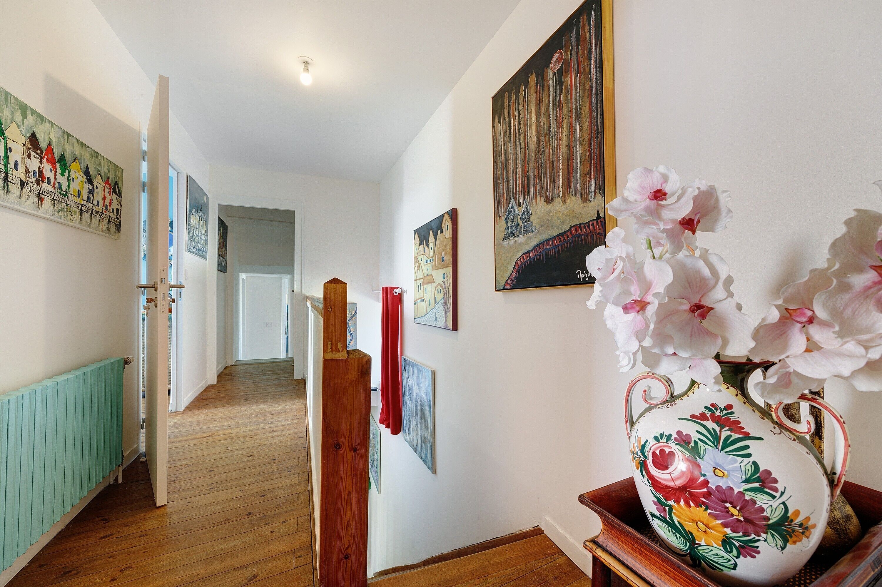 Ein Flur mit Holzböden, weißen Wänden und verschiedenen Kunstwerken.