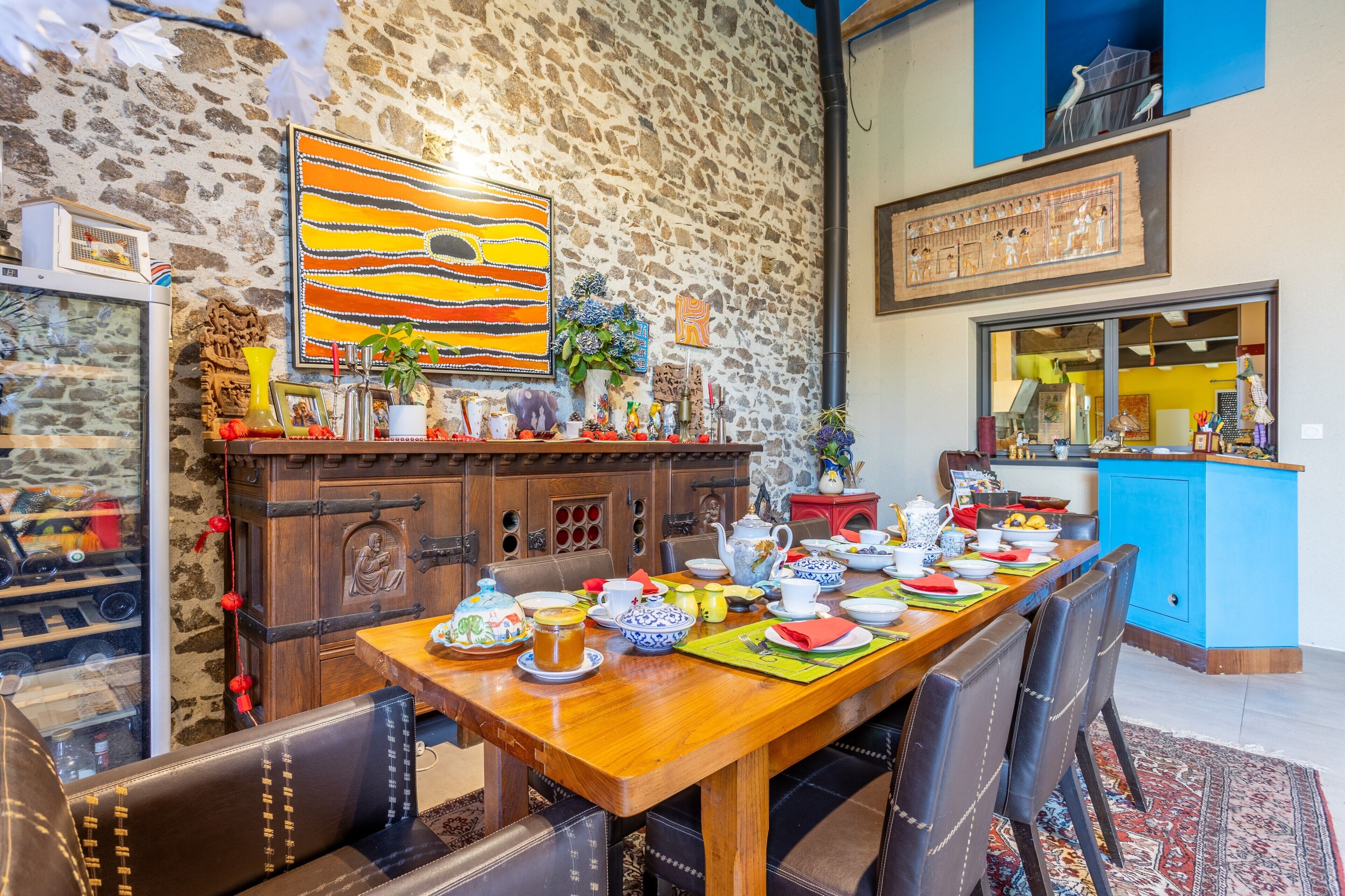 Un espace repas avec une longue table en bois dressée pour un repas, entouré de murs en pierre et agrémenté de divers objets décoratifs.