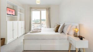 A bedroom with a bed, a TV on a shelf, and a window with curtains.