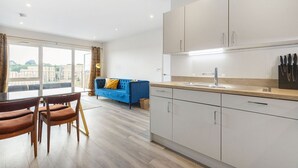 A modern kitchen with white cabinets, a wooden countertop, and a built-in sink. There is a dining area with a table and chairs, and a blue sofa in the background.