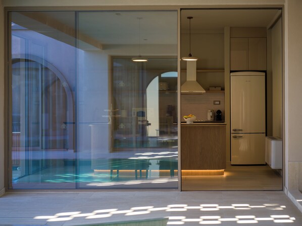 A modern kitchen with a built-in refrigerator, a dining area with a glass partition, and a view of the outside. - The Landmark Villas & Spa (Rhodes)