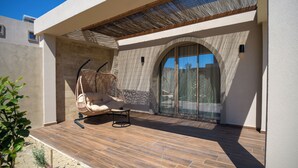 A modern outdoor patio with a wicker chair, a small table, and a glass door leading to a covered area. - The Landmark Villas & Spa (Rhodes)