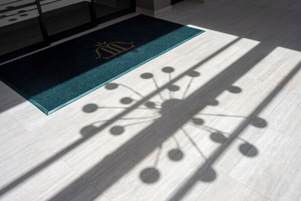A doormat with a logo, a shadow pattern on the floor, and a light-colored floor. - The Landmark Villas & Spa (Rhodes)