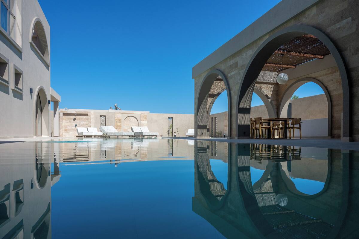 Una piscina con agua cristalina, sillas de descanso y una zona de comedor con mesas y sillas.