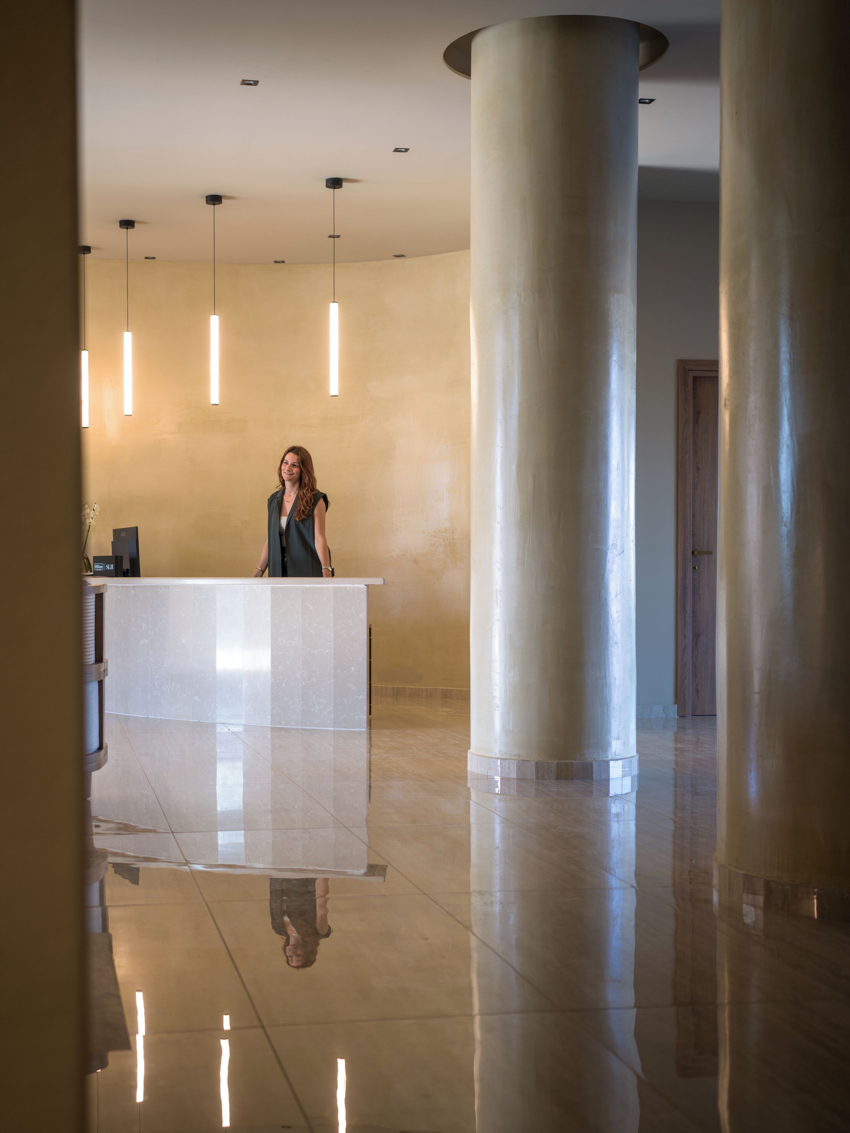 Un área de recepción con mostrador de mármol, columnas imponentes e iluminación colgante.