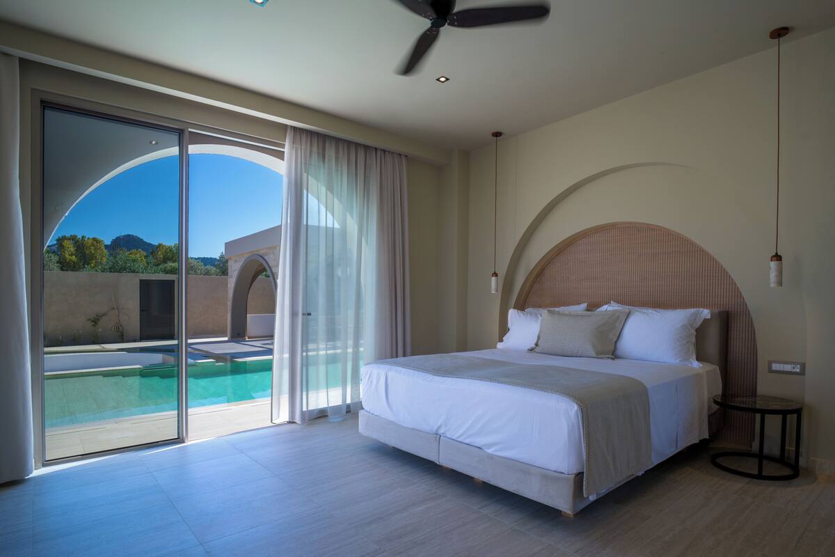 Un dormitorio con cama, ventilador de techo, vista a una piscina y un ventanal grande.