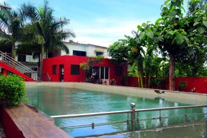 Ein Swimmingpool mit einem roten Gebäude im Hintergrund, umgeben von viel Grün.