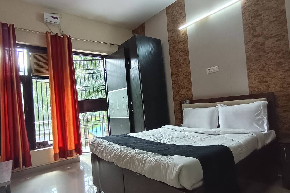 A hotel room with a bed, a wardrobe, a window with curtains, and an air conditioning unit.