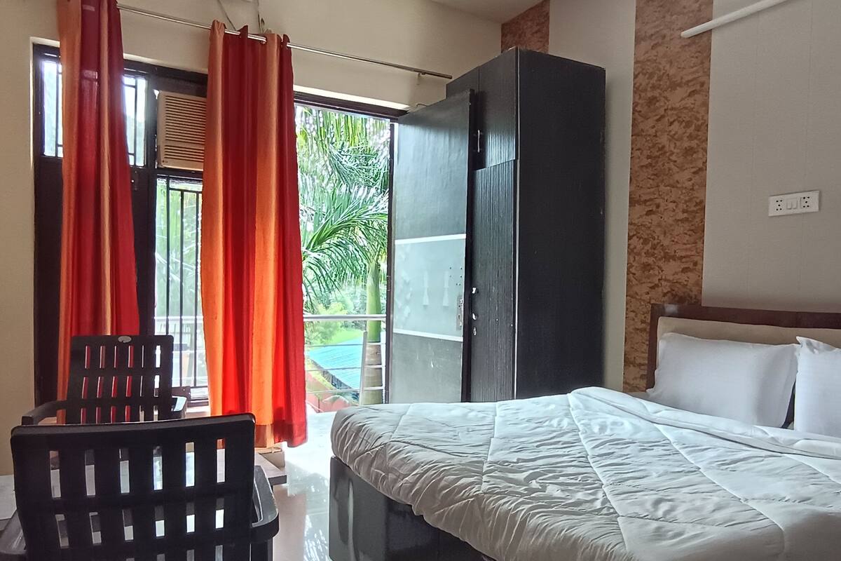 A hotel room with a bed, a wardrobe, a chair, and a view of the outdoors.