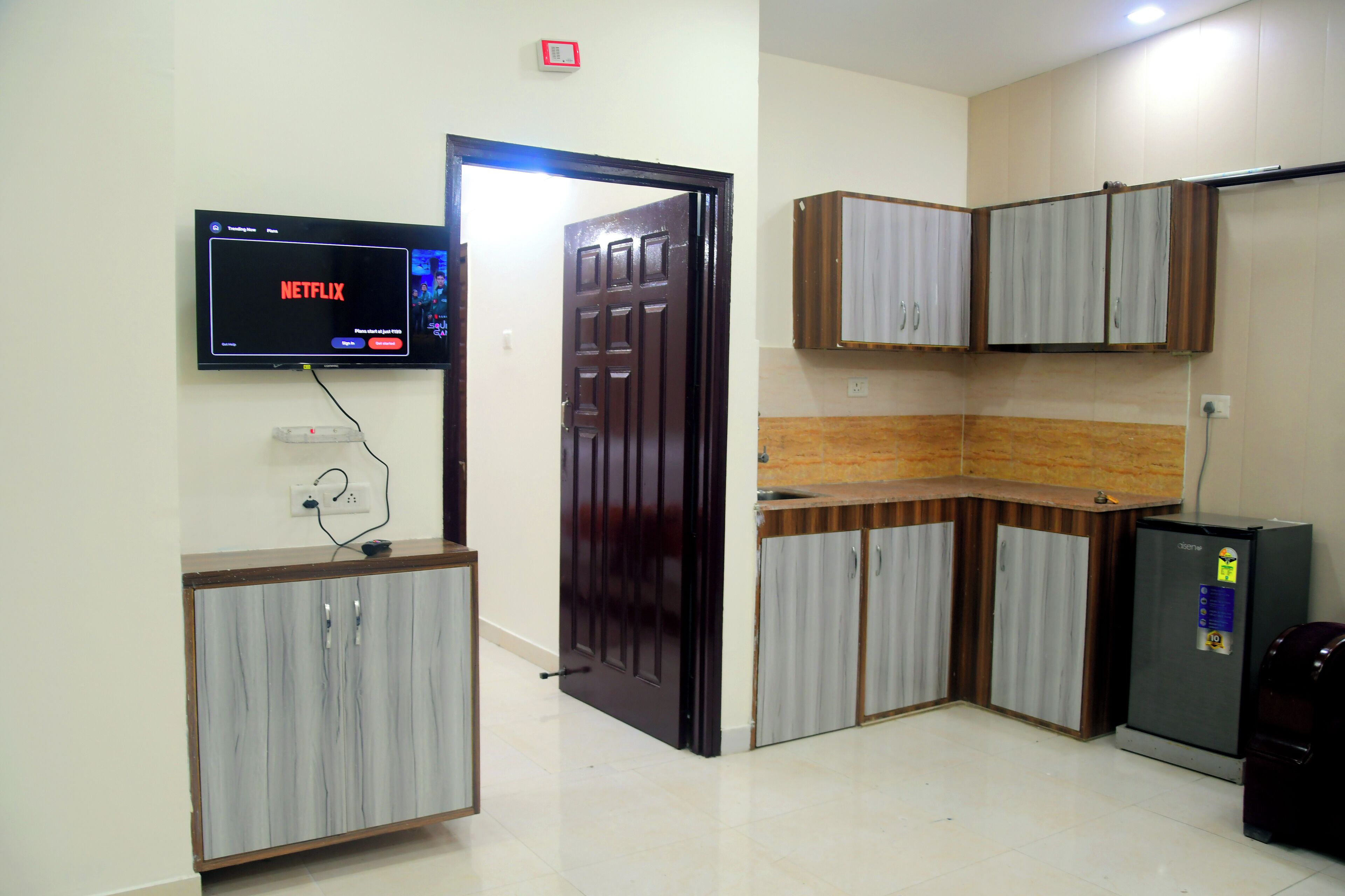 Ein Zimmer mit Fernseher, der Netflix anzeigt, einem Kühlschrank und eingebauten Schränken.