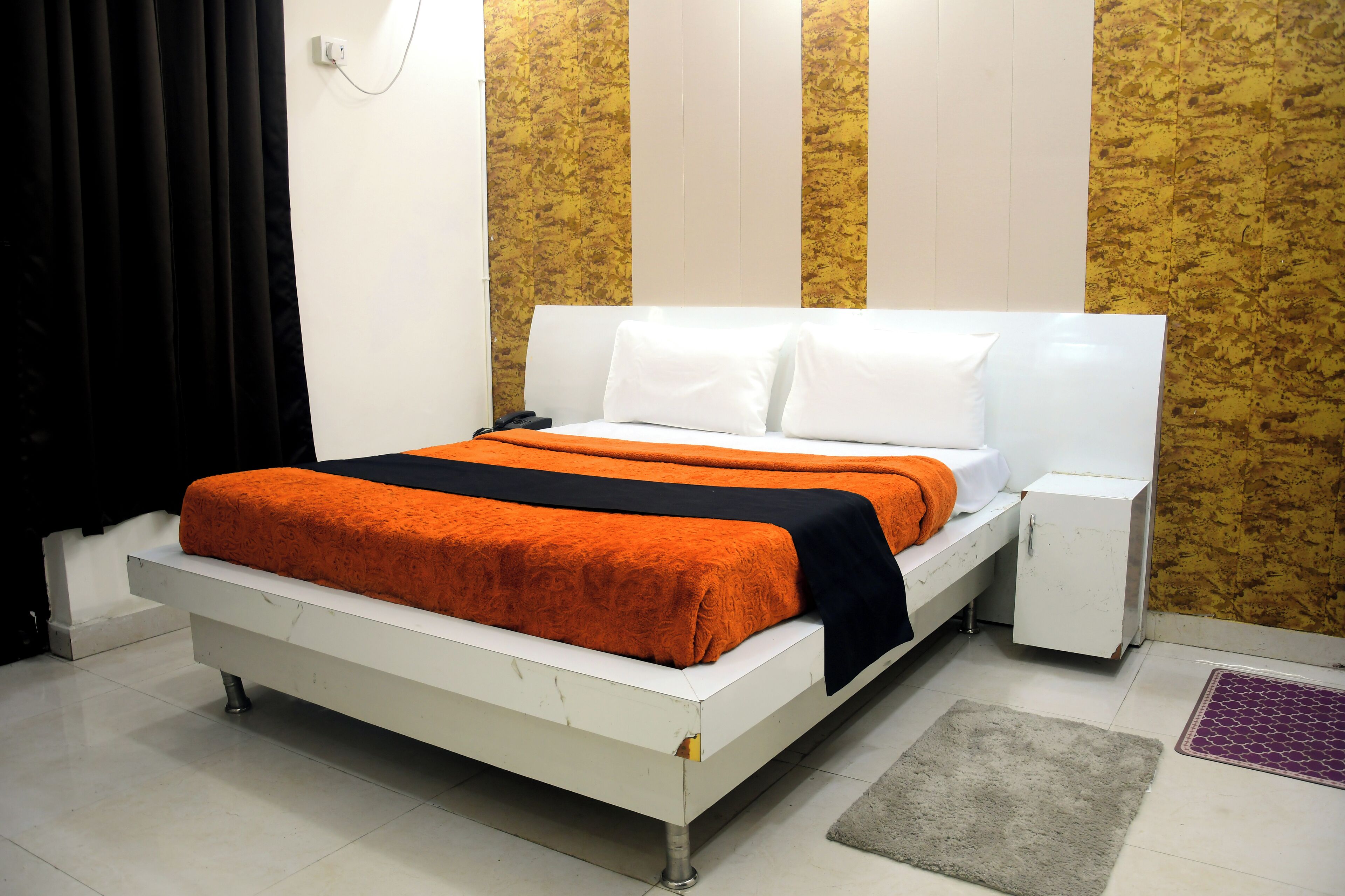 A bed with white and orange bedding, a bedside table, and a wall with vertical stripes.
