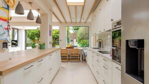 A modern kitchen with white cabinets, a wooden countertop, and a dining area with a table and chairs. - Spacious 4B family home by Richmond riverside (Twickenham)