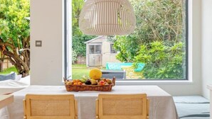 A room with a large window, a table with a fruit basket, two wicker chairs, and a hanging light fixture. - Spacious 4B family home by Richmond riverside (Twickenham)