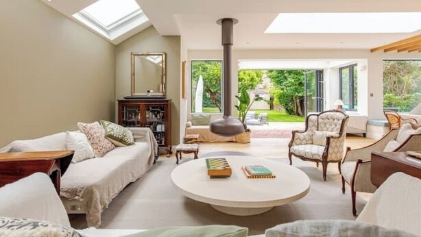 A spacious living room with a round coffee table, comfortable seating, and a large window offering a view of the garden. - Spacious 4B family home by Richmond riverside (Twickenham)