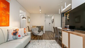 Uma sala de estar moderna com sofá, mesa de jantar e área de cozinha equipada com geladeira e televisão.