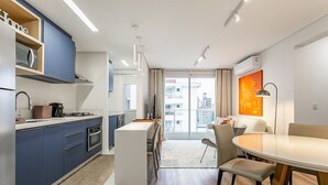 Uma cozinha moderna com micro-ondas embutido, fogão e pia. Há uma área de refeições com uma mesa redonda e cadeiras.