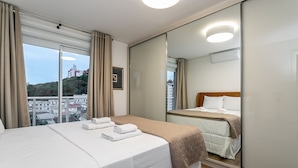 Quarto de hotel com uma cama, mesa de cabeceira, espelho e janela com cortinas.