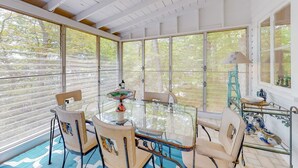 A sunlit room with a glass table, chairs, and a view of trees through large windows. - Mashpee Heaven Lake front (Mashpee)