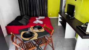 Una habitación compacta con cama, una mesa de comedor con sillas, televisión y una pequeña cocina.