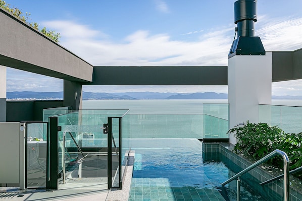 A modern infinity pool with a glass barrier, a telescope, and a view of mountains.