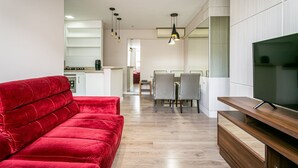 Ein modernes Wohnzimmer mit einem roten Sofa, einem TV-Schrank aus Holz und einem Essbereich im Hintergrund.