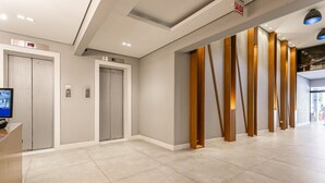 Eine moderne Hotelhalle mit Aufzügen, einer Rezeption und einem großen digitalen Bildschirm.