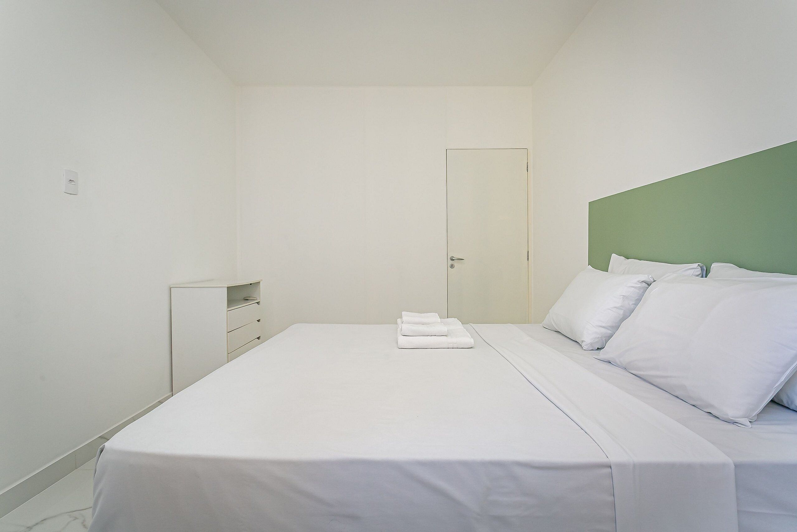 A minimalist bedroom with a bed, a nightstand, and a door.