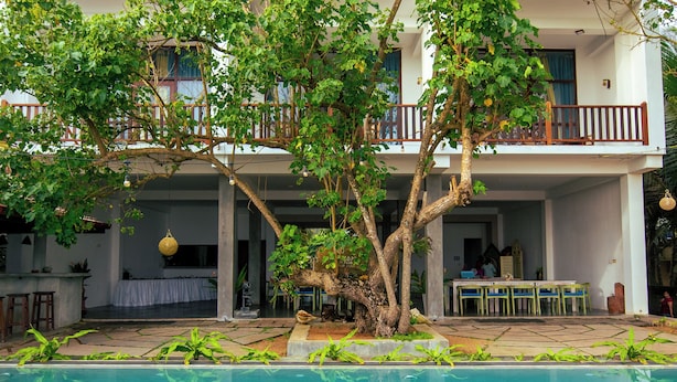 Ein zweistöckiges Gebäude mit Balkon, Pool und Essbereich mit Gartenmöbeln.