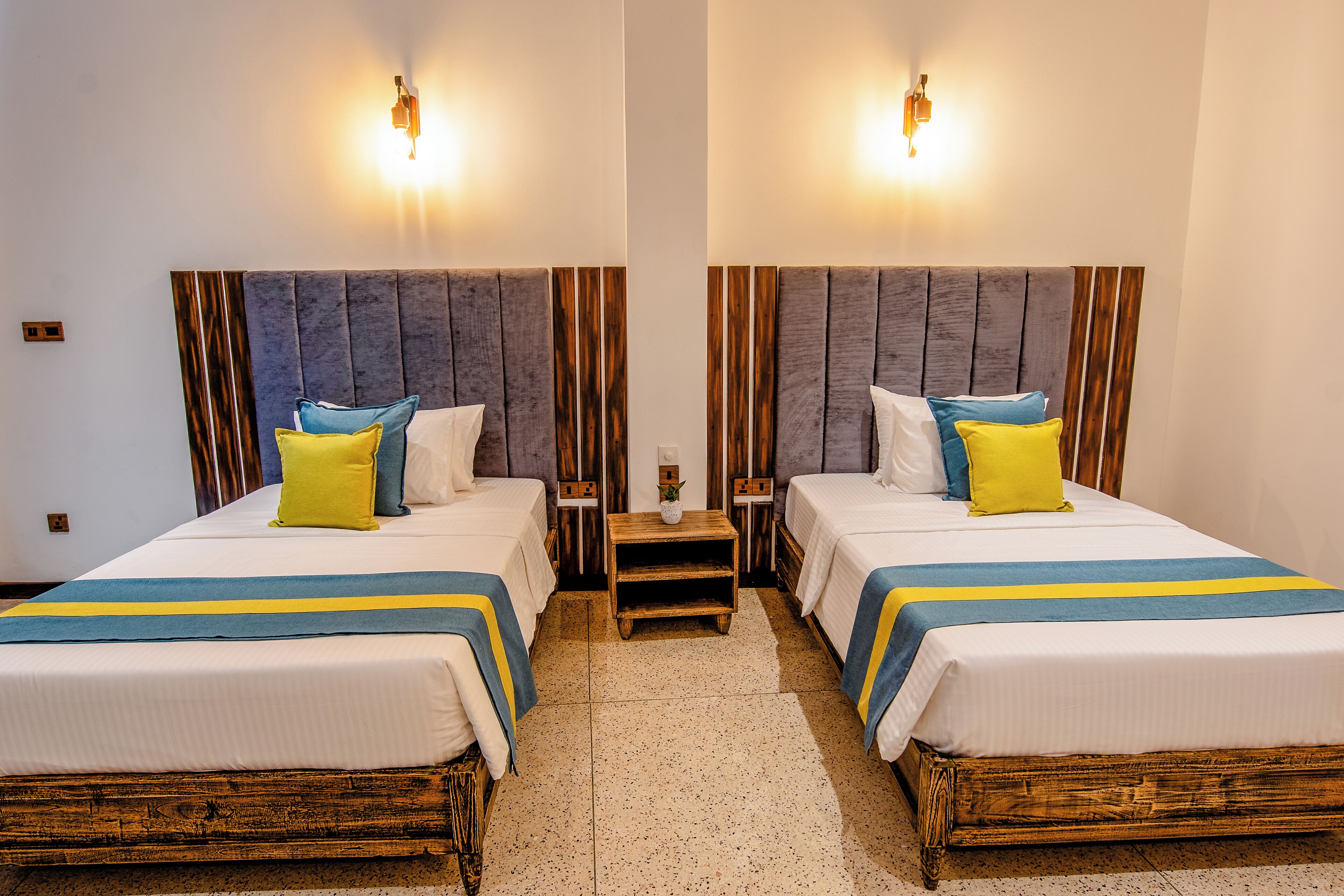 Ein Zimmer mit Spiegel und zwei Betten, jeweils mit einem hölzernen Kopfteil, weißer Bettwäsche und blau-gelben Akzenten.