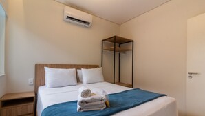 Una cama bien hecha con un edredón azul, almohadas blancas y toallas dobladas a un lado.