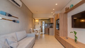 Una sala de estar moderna con un sofá, una mesa de comedor con sillas, una zona de cocina con refrigerador y un televisor montado en la pared.