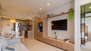 Una sala de estar moderna con sofá, televisor y área de cocina con armarios de madera y microondas.