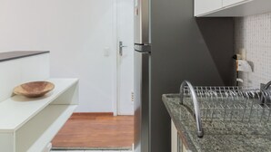 A kitchen with white cabinets, a stainless steel refrigerator, a granite countertop, and a wooden bowl on a white shelf.