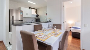 A compact kitchen with a refrigerator, microwave, and stove. There is a dining table with chairs and a small table lamp.