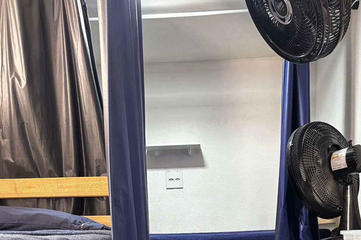 Un dormitorio con literas, un escritorio con computadora y un ventilador de pie.