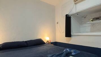 A single bed with a dark blue blanket and pillows, a bedside lamp, and a wall-mounted air conditioning unit.