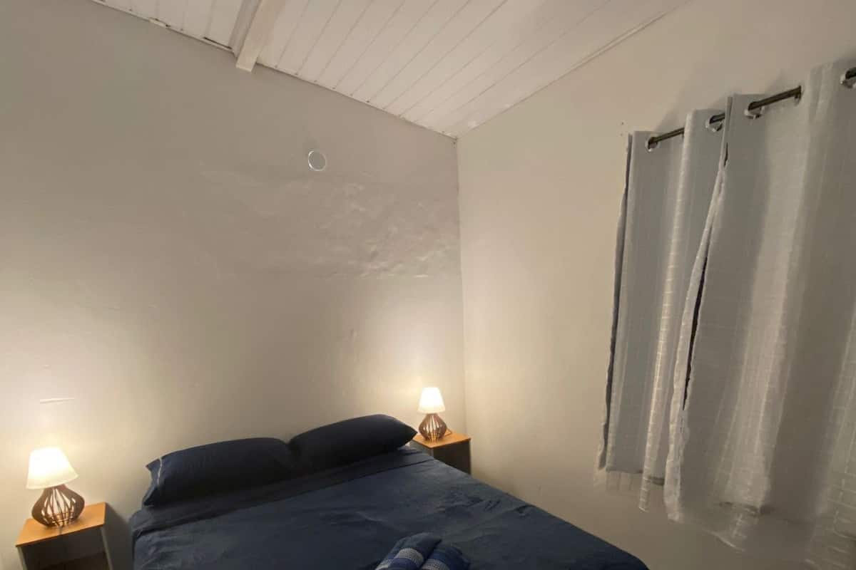 Una cama individual con colcha azul oscuro, dos lámparas de noche y una cortina en la ventana.