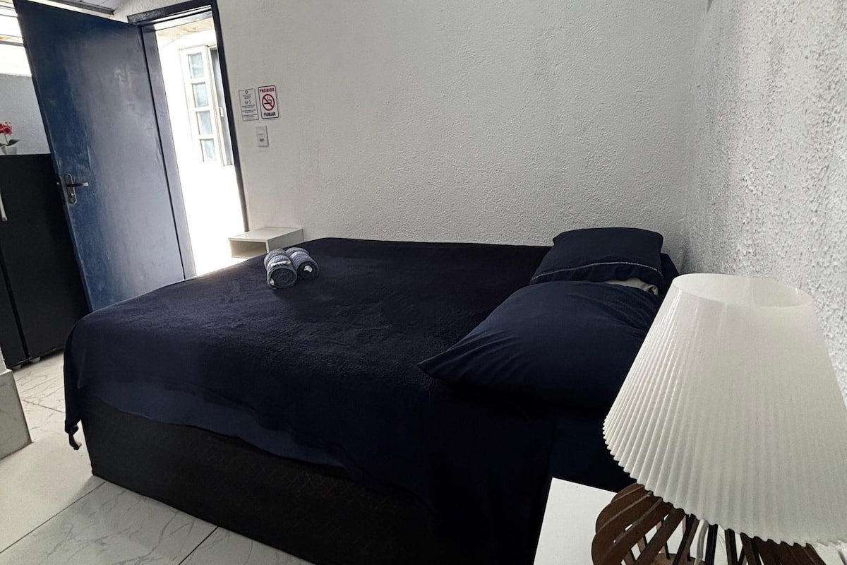 Un dormitorio con cama, lámpara de noche y puerta que da a otra habitación.