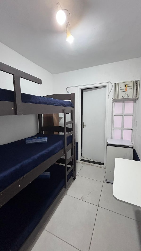 A dormitory room with bunk beds, a desk, a chair, a radiator, and a door.