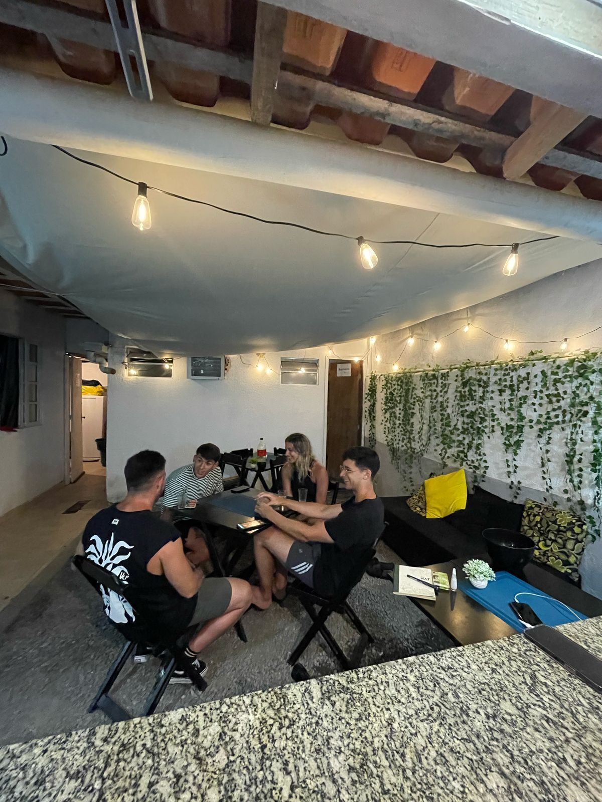 A group of people seated around a table in a room with a high ceiling, exposed beams, and string lights.