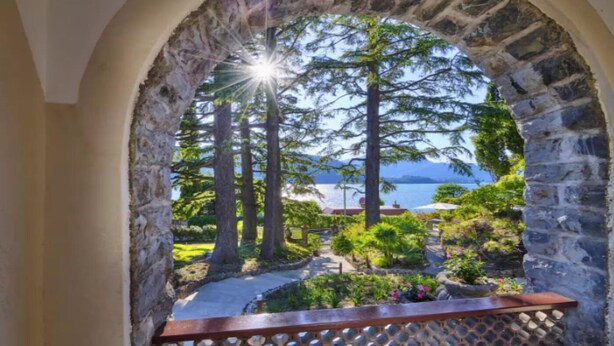 An arched stone structure with a view of a garden and a body of water. - Elegant Historic Villa with Pool, Jacuzzi & Lake Views in Lierna (Lierna)