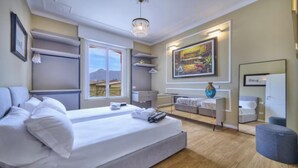 A modern hotel room with a large bed, a desk, a chair, and a window with a view of mountains. - Elegant Historic Villa with Pool, Jacuzzi & Lake Views in Lierna (Lierna)