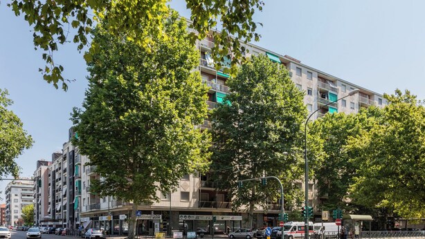 Un edificio de varios pisos con zona comercial en la planta baja, que incluye un bar y diversas tiendas.