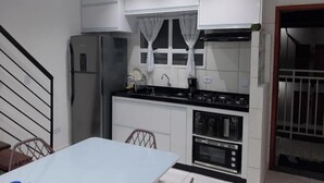 Uma cozinha compacta com armários brancos, uma geladeira de aço inoxidável, um fogão a gás e um micro-ondas.