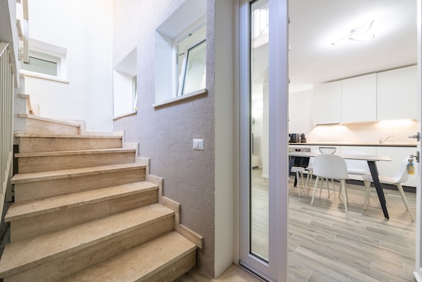 Un interior moderno con una escalera que conduce a un comedor, una cocina con armarios blancos y un ventanal corredero.
