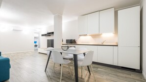 Une cuisine moderne avec des meubles blancs, une table à manger avec des chaises et un canapé bleu.