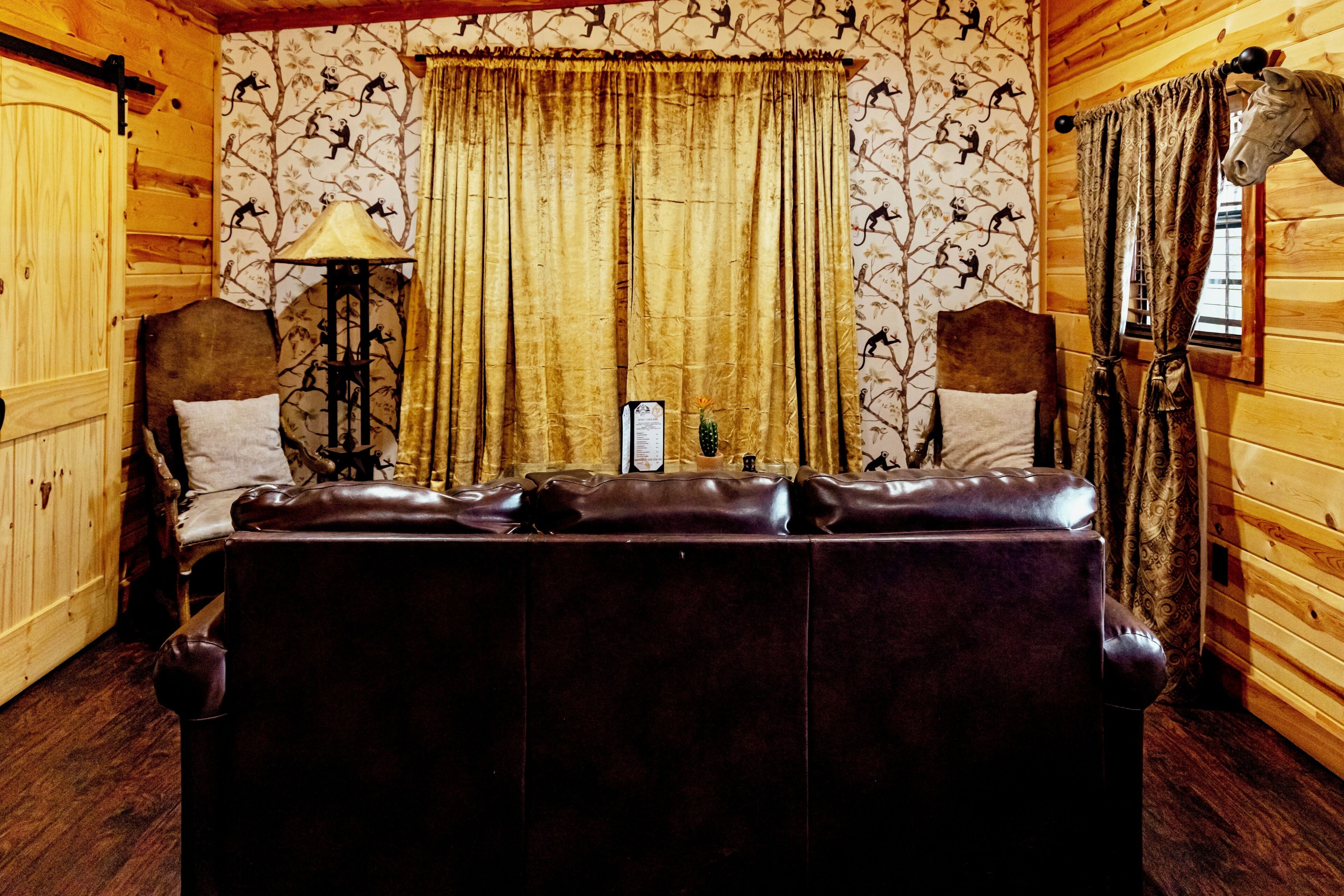 A log cabin interior with a leather sofa, curtains, a lamp, and a wall with monkey wallpaper.