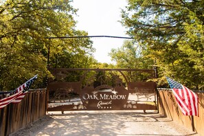 A wooden gate with the sign "Oak Meadow Ranch" and two American flags on either side.