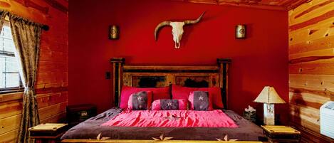 A wooden cabin room with a bed, red walls, a wooden ceiling, and a cow skull on the wall.